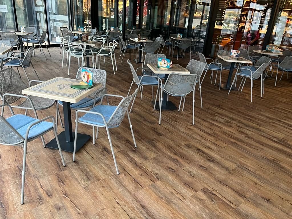 Terrasse eines Restaurants mit Tischen und Stühlen auf Boden in Holzoptik