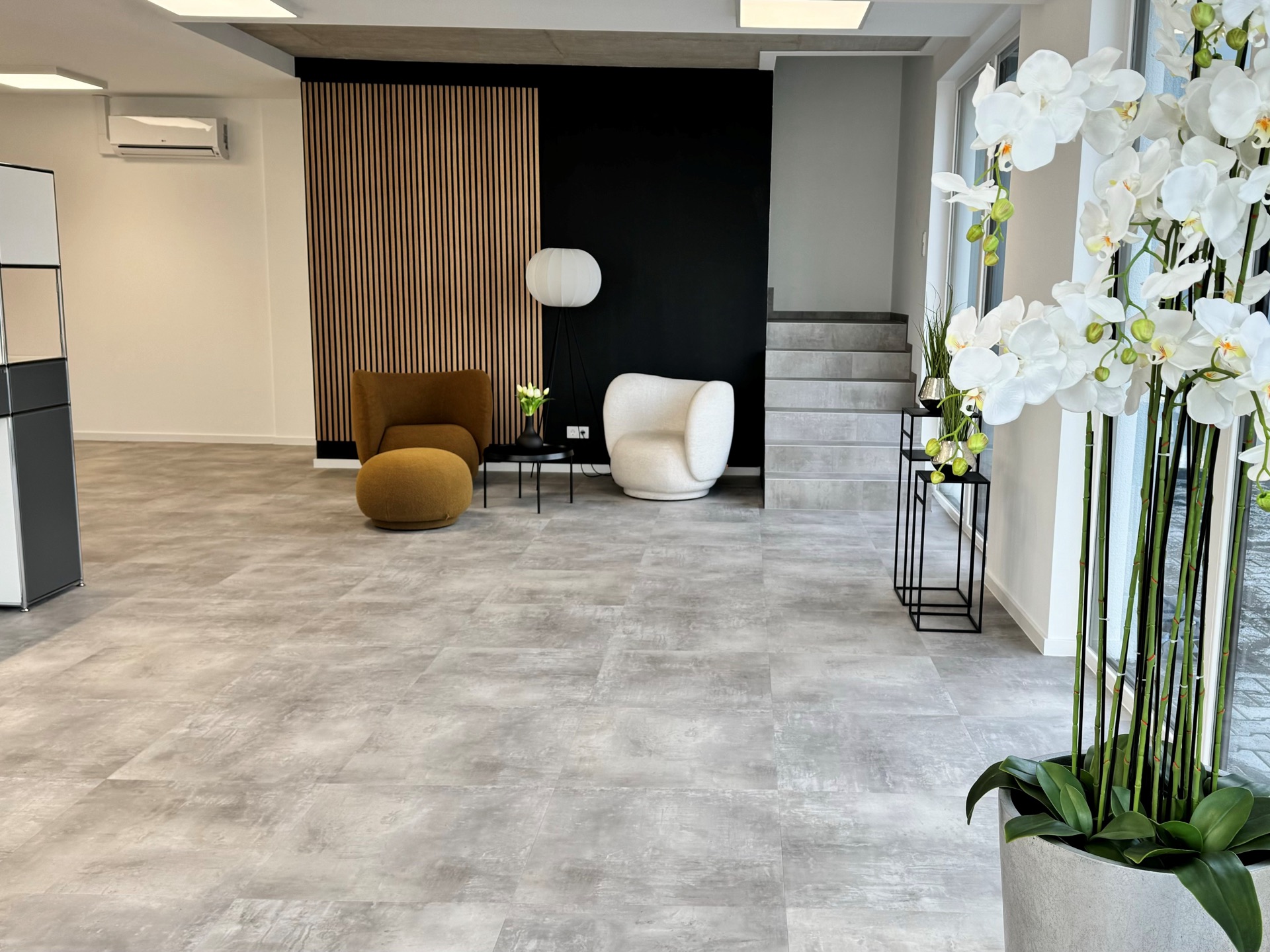 Empfangsbereich mit hellem Designboden in Zementoptik, Holzlamellenwand und Sitzgruppe